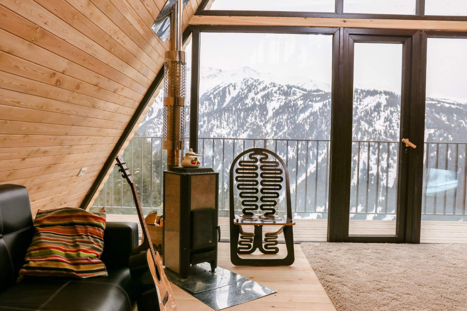 Cozy cabin interior with a wood-burning stove overlooking snowy mountain peaks.