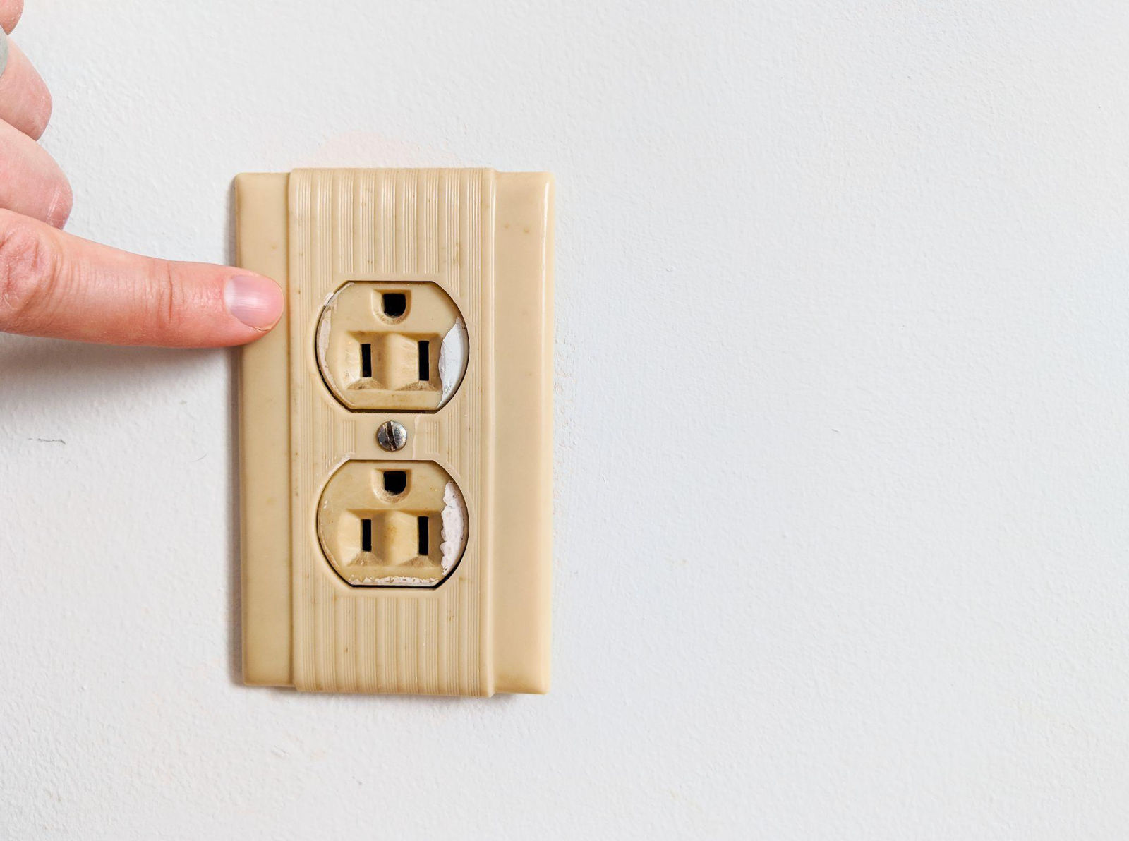 Person pointing to an old wall outlet to inspect for wear before winterizing a cabin.