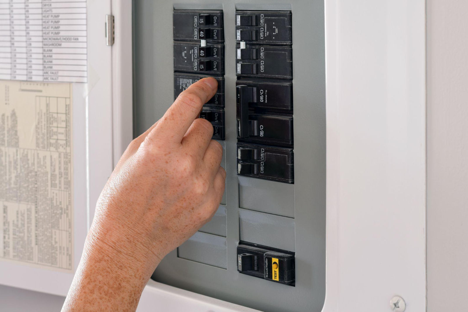 Hand flipping a circuit breaker switch inside an open electrical panel door.